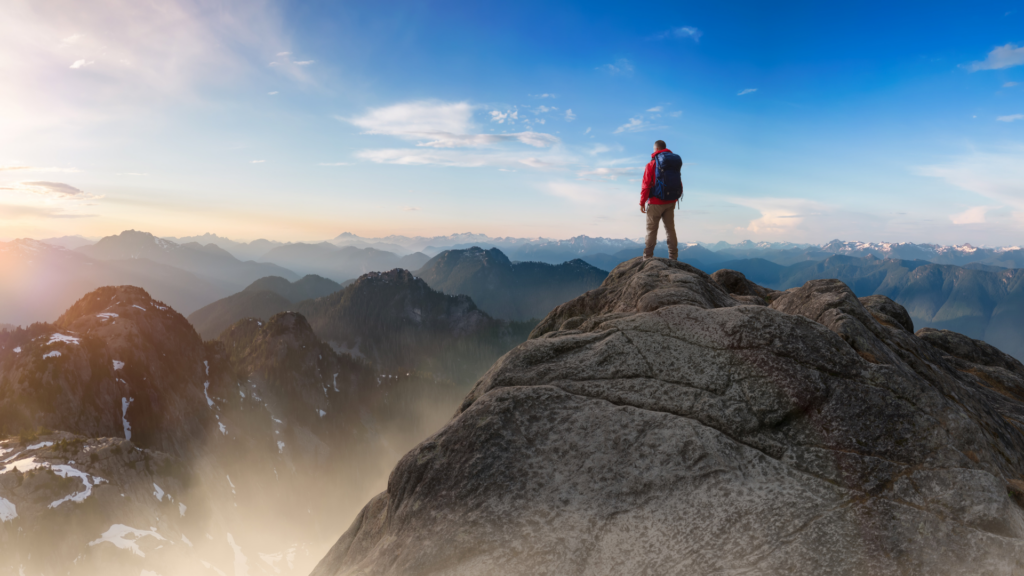 Person standing triumphantly on a mountain peak at sunrise, symbolizing success and the power of positive thinking.