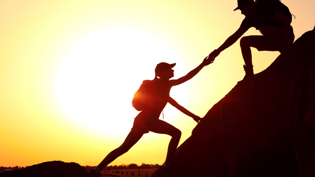 An inspiring image of two individuals supporting each other to climb a steep hill, symbolizing teamwork and overcoming challenges through positivity.